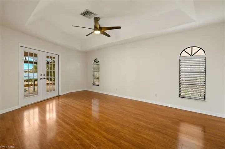 Unfurnished room featuring a raised ceiling, french doors, wood finished floors, and a ceiling fan