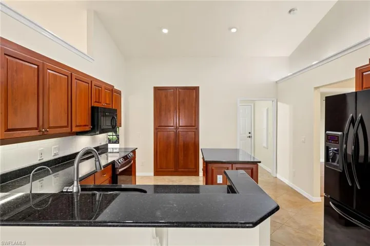 Kitchen featuring a kitchen island, black refrigerator with ice dispenser, dark stone countertops, light tile patterned floors, and recessed lighting