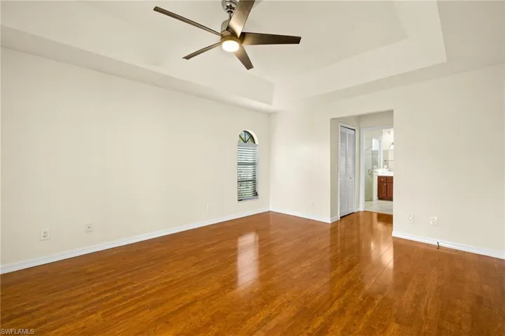 Unfurnished room featuring a tray ceiling, dark wood-style floors, and ceiling fan