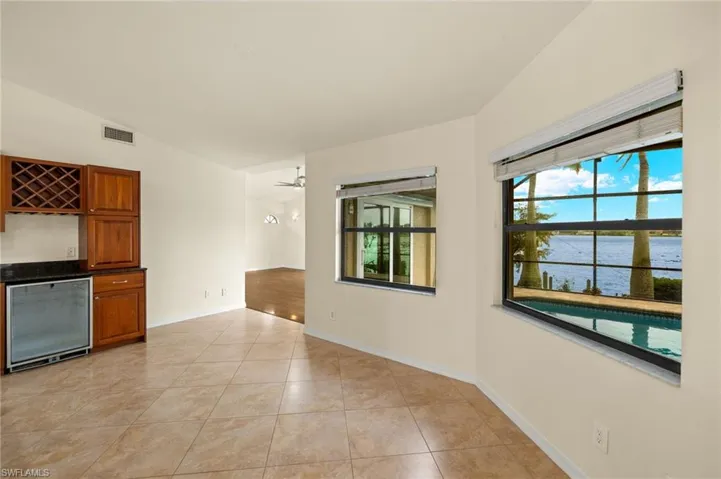 Empty room featuring a water view, light tile patterned flooring, lofted ceiling, and a dry bar