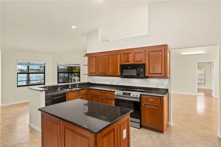 Kitchen featuring black appliances, brown cabinetry, light tile patterned flooring, a center island, and a peninsula