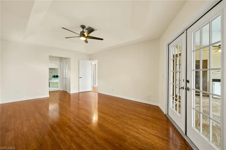 Empty room with a ceiling fan, a raised ceiling, dark wood-type flooring, and french doors