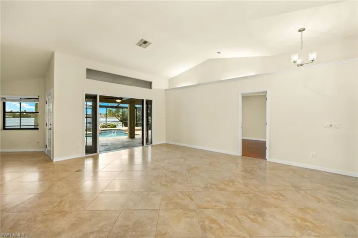 Empty room with lofted ceiling, a chandelier, and light tile patterned flooring
