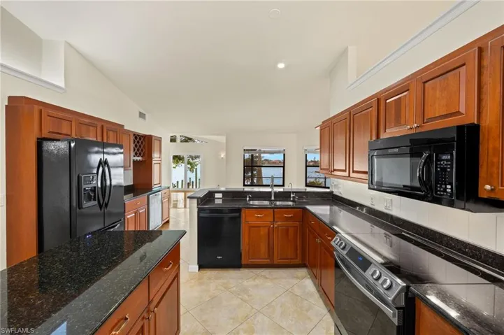 Kitchen with black appliances, brown cabinetry, light tile patterned floors, vaulted ceiling, and recessed lighting