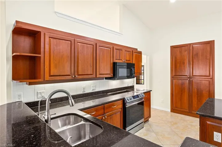 Kitchen featuring backsplash, stainless steel electric stove, open shelves, dark stone counters, and black microwave