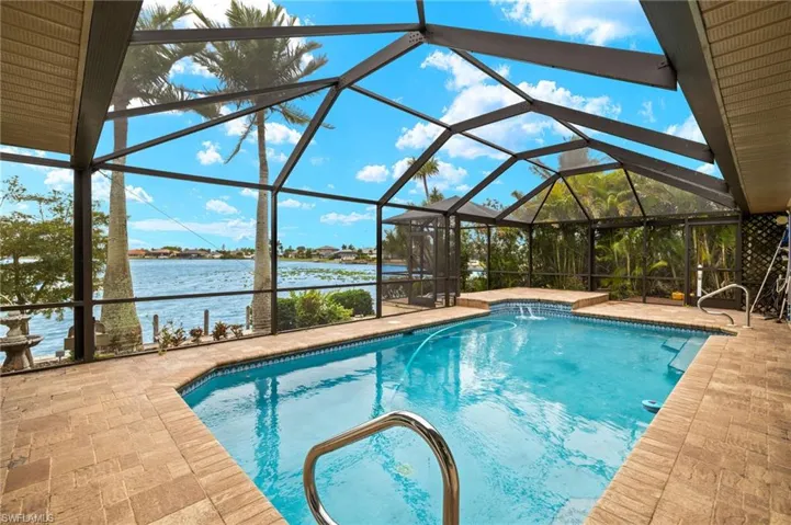 Outdoor pool with glass enclosure, a water view, a sunroom, and a patio