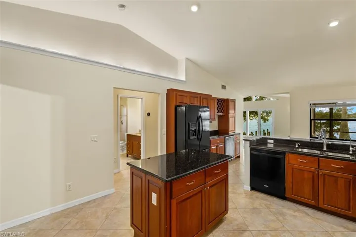 Kitchen featuring lofted ceiling, dark stone countertops, black appliances, a kitchen island, and light tile patterned flooring