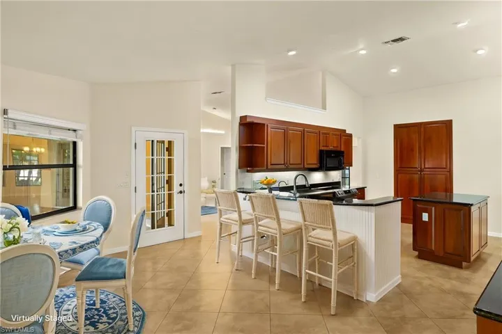 Kitchen with a kitchen breakfast bar, light tile patterned floors, open shelves, black microwave, and brown cabinetry