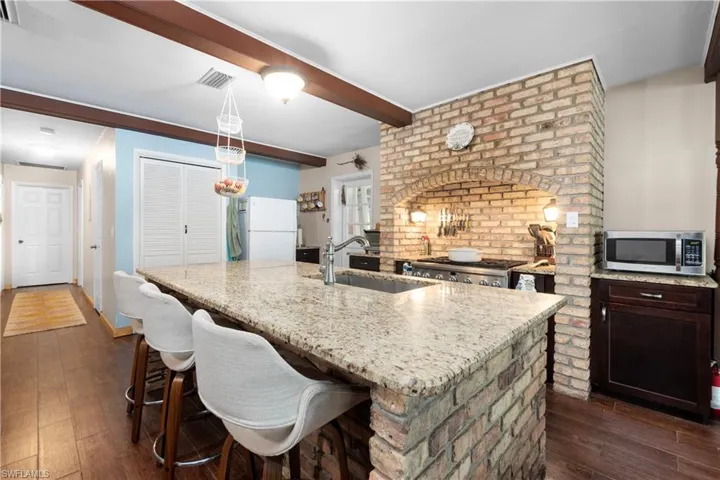 Kitchen with white refrigerator, sink, dark wood-type flooring, beam ceiling, and a kitchen island with sink