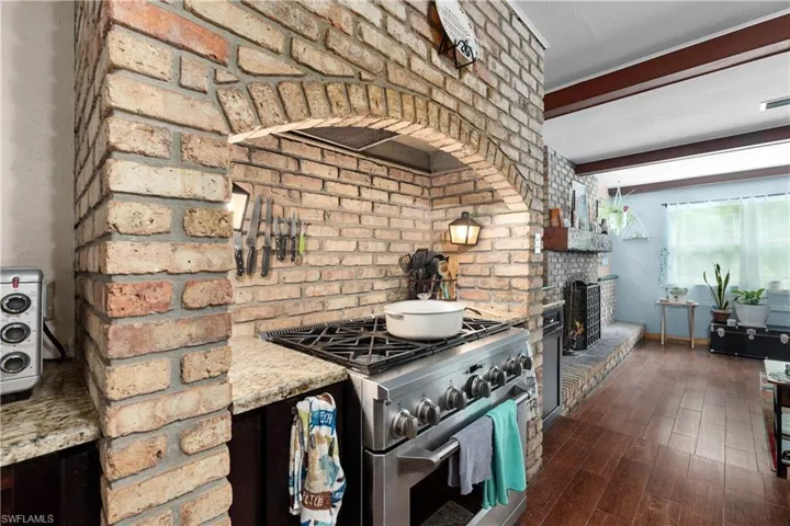 Kitchen featuring dark hardwood / wood-style floors, brick wall, stainless steel range, and beam ceiling