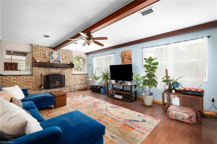 Living room with hardwood / wood-style flooring, ceiling fan, beamed ceiling, brick wall, and a brick fireplace