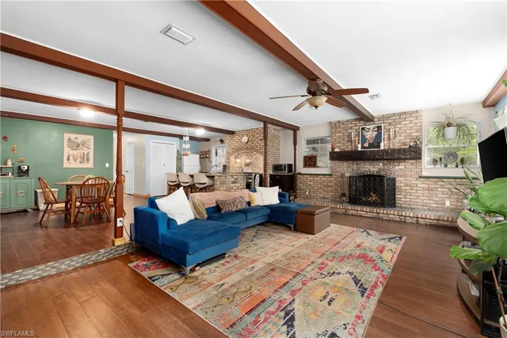 Living room featuring a fireplace, ceiling fan, dark hardwood / wood-style flooring, brick wall, and beam ceiling