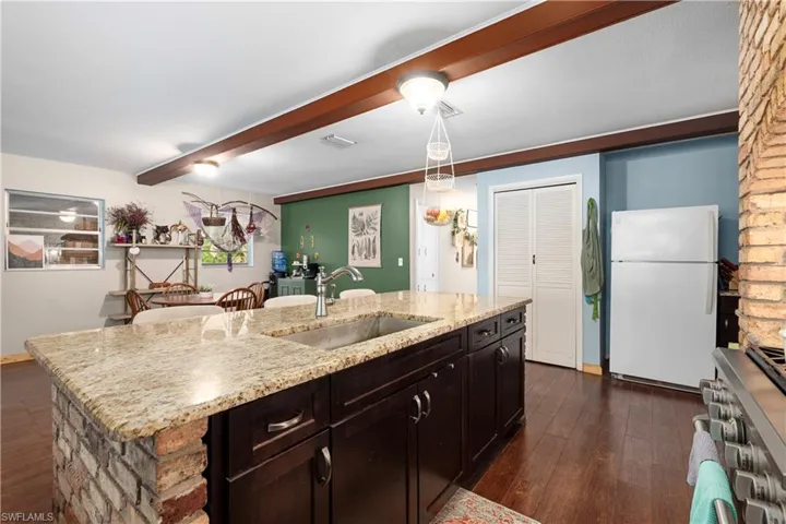 Kitchen with dark wood-type flooring, an island with sink, beamed ceiling, white refrigerator, and sink