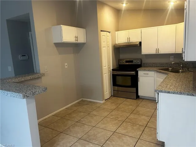 Kitchen with white cabinetry, stainless steel range with electric stovetop, high vaulted ceiling, sink, and light tile floors
