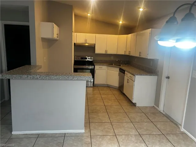 Kitchen featuring white cabinets, vaulted ceiling, appliances with stainless steel finishes, and light tile flooring