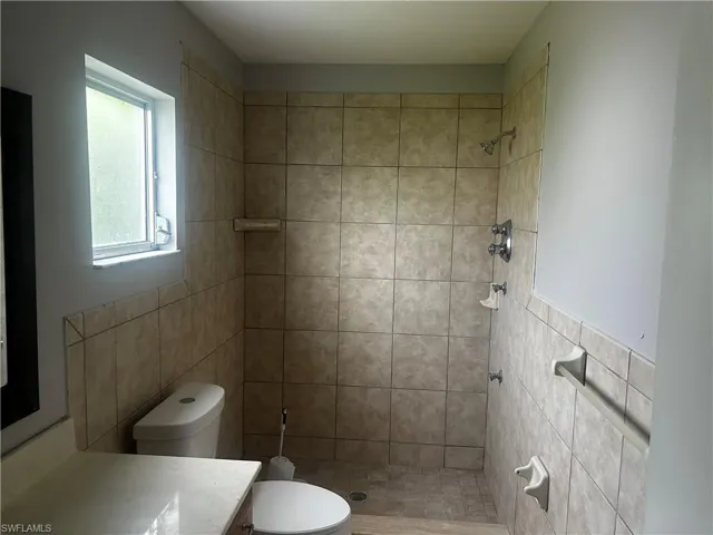 Bathroom featuring tile walls, tiled shower, toilet, and vanity