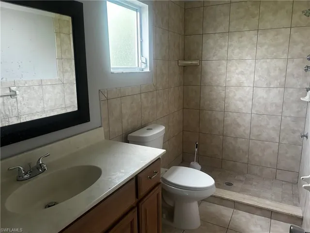 Bathroom featuring tile floors, tile walls, a tile shower, toilet, and vanity