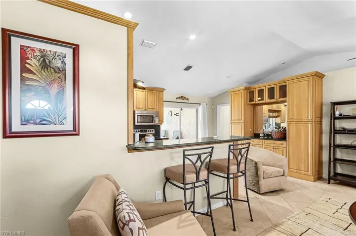 Kitchen with a breakfast bar, lofted ceiling, stainless steel appliances, a peninsula, and glass insert cabinets