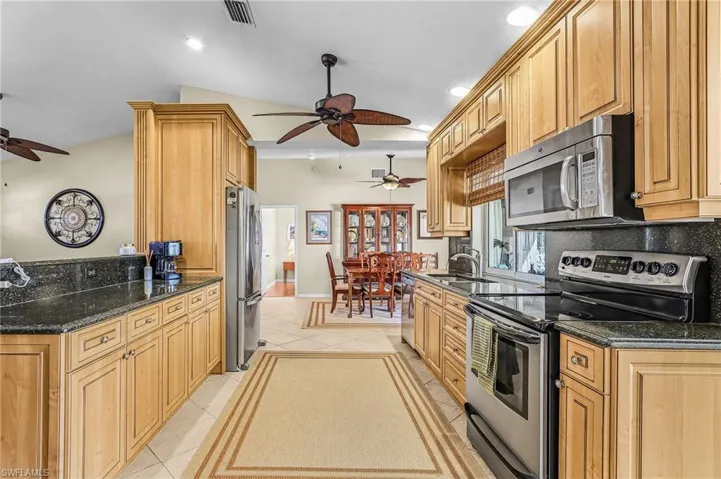 Kitchen with stainless steel appliances, ceiling fan, dark stone counters, light tile patterned flooring, and recessed lighting
