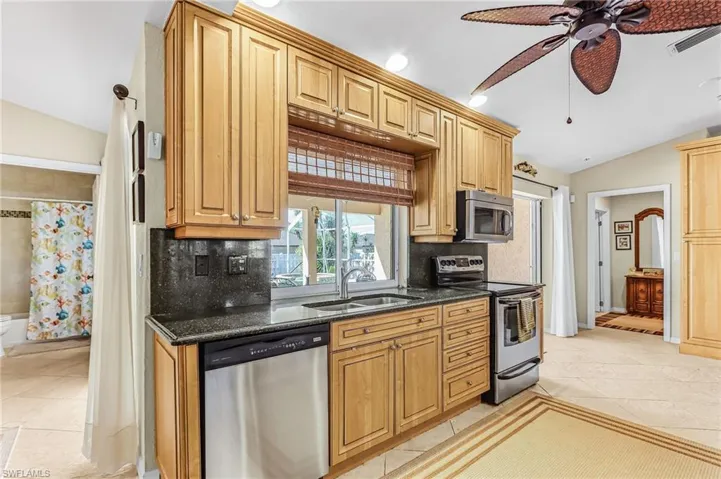 Kitchen with lofted ceiling, stainless steel appliances, dark stone countertops, light tile patterned floors, and a ceiling fan