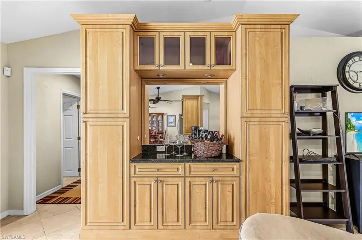 Kitchen featuring glass insert cabinets, dark stone counters, lofted ceiling, light tile patterned flooring, and light wood finish cabinetry