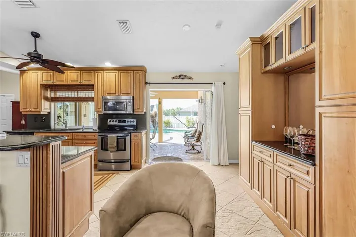 Kitchen featuring dark stone counters, stainless steel appliances, glass insert cabinets, a ceiling fan, and recessed lighting