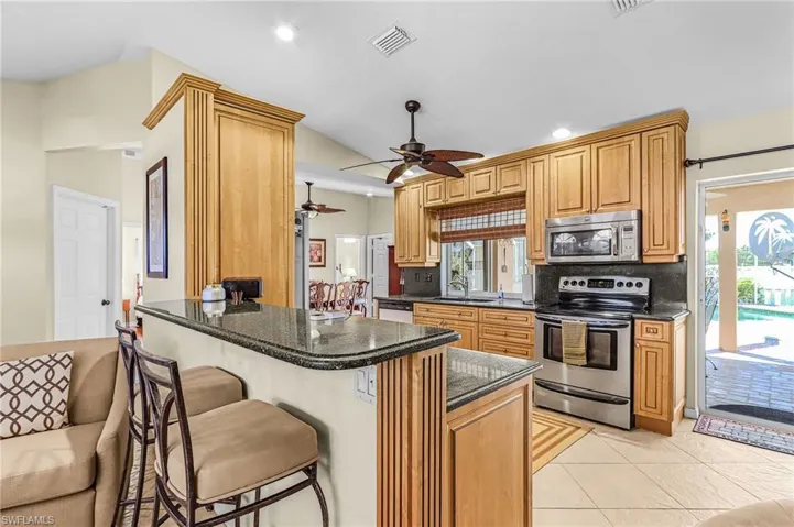 Kitchen featuring stainless steel appliances, dark stone countertops, a breakfast bar, light tile patterned floors, and a peninsula