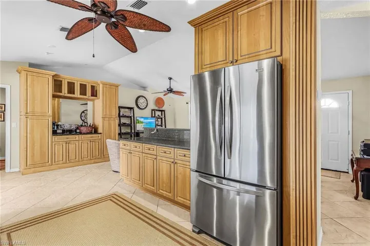 Kitchen featuring freestanding refrigerator, dark stone counters, lofted ceiling, ceiling fan, and light tile patterned flooring