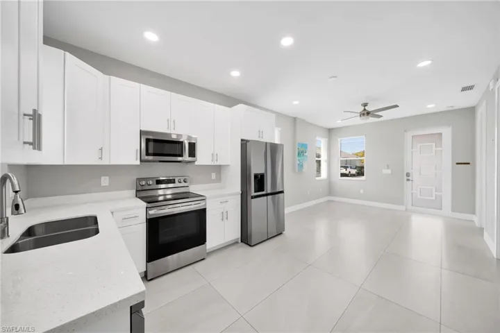 Kitchen featuring stainless steel appliances, recessed lighting, white cabinetry, light stone countertops, and ceiling fan