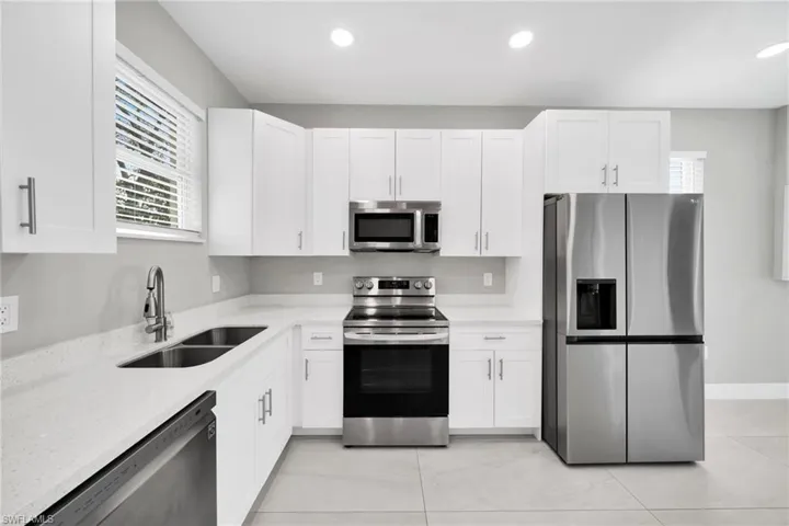 Kitchen featuring stainless steel appliances, light stone countertops, white cabinets, recessed lighting, and plenty of natural light