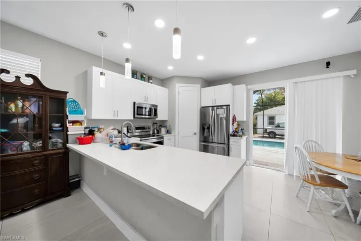 Kitchen featuring stainless steel appliances, a peninsula, white cabinets, hanging light fixtures, and light stone countertops