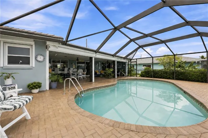 Screened-in outdoor living space with a curved swimming pool, integrated pool steps, and a paver deck