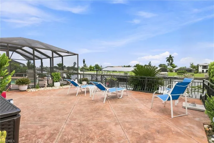 Spacious outdoor patio with stamped concrete flooring, screened enclosure, and a wrought iron railing overlooking a canal