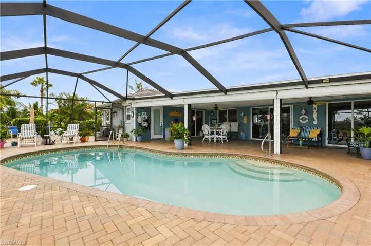 Screened pool enclosure featuring a curvilinear pool, paver patio, covered porch, and multiple glass doors