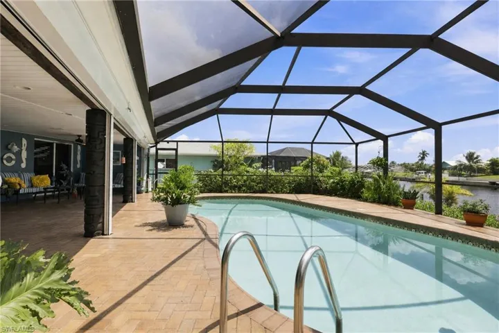 Screened outdoor pool with a curved edge, brick paver decking, built-in planters, and an open-air living area