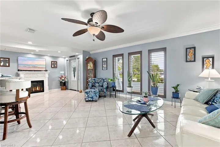 White tile flooring, ceiling fan with integrated lighting, recessed lighting, white mantel fireplace, and plantation shutters