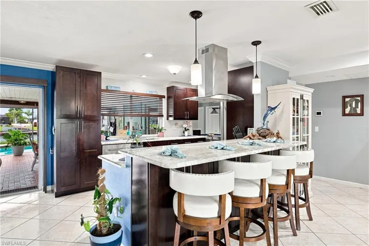 Kitchen featuring an island with stone countertops, dark wood-finish cabinetry, stainless steel range hood, and tile flooring