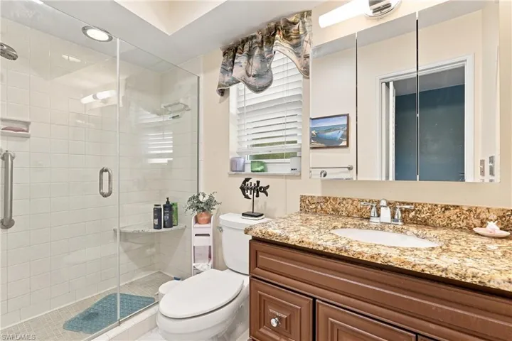 Spa-inspired primary bathroom featuring a frameless glass-enclosed shower with subway tile surround, dual-sink vanity with granite countertop, wood-finish cabinetry, and recessed ceiling lighting
