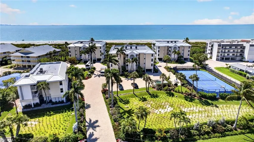 The property features several buildings with white exteriors and gray roofs, surrounded by lush green landscaping and palm trees
