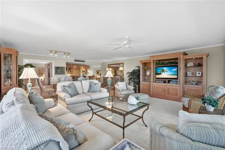 Spacious living area featuring carpet flooring, a ceiling fan, and a large custom built-in entertainment center with storage and display shelving