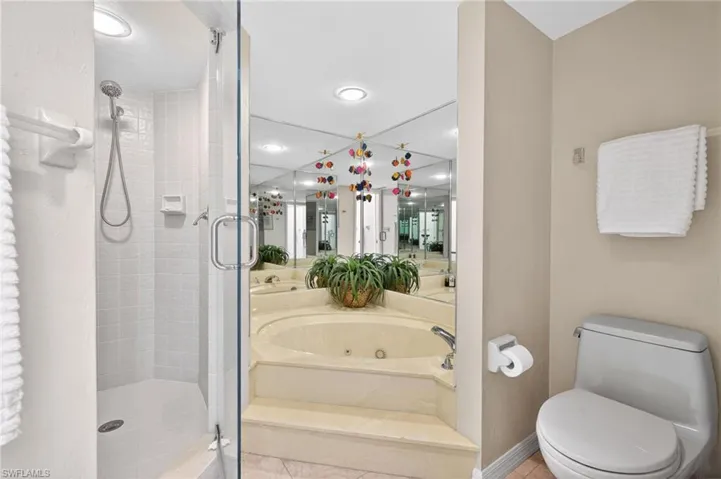 Primary Bathroom features a walk-in shower with a glass enclosure, a built-in corner bathtub, a toilet, and wall-mounted mirrors