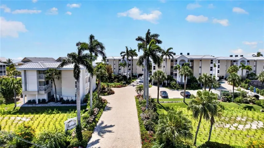 The property features an extensive driveway, surrounded by mature palm trees and manicured landscaping, leading to a multi-story building with balconies