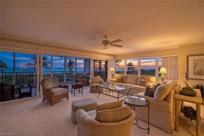 Living area features expansive sliding glass doors and windows, offering panoramic views of the ocean and sunset