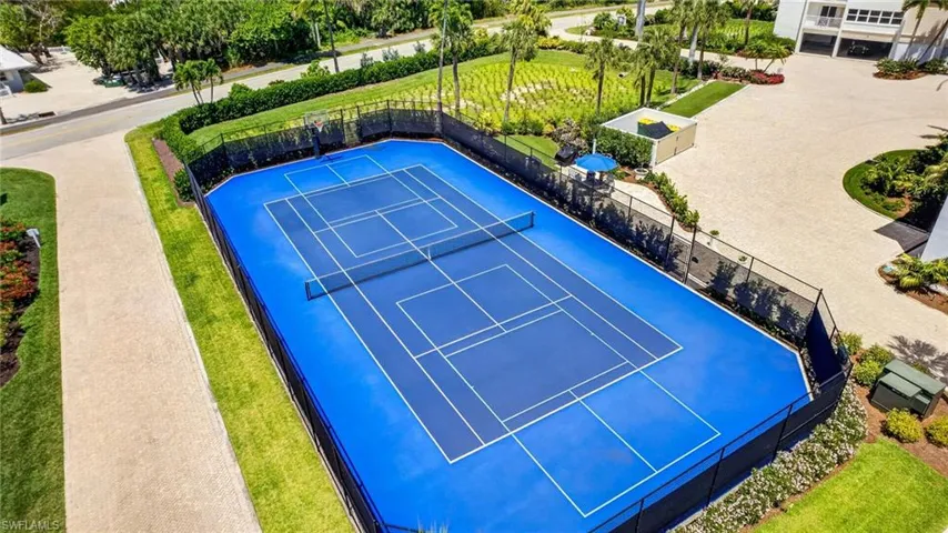 A vibrant blue tennis court is a prominent feature, enclosed by a fence and surrounded by well-maintained landscaping