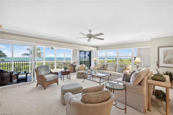 Living area featuring expansive windows with ocean views, light-colored carpeting, and a ceiling fan