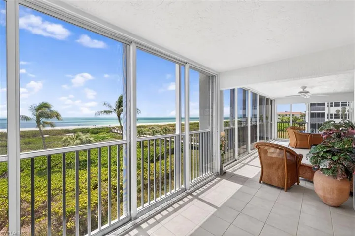 This screened lanai features a tiled floor, a ceiling fan, and offers expansive views of the beach and ocean