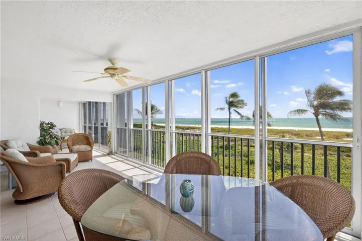 The enclosed porch features large windows offering extensive views of the beach and ocean, a ceiling fan, and tiled flooring
