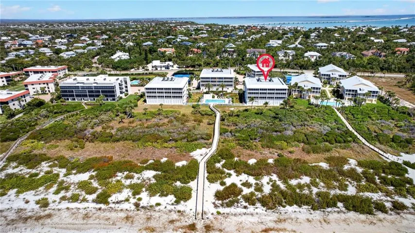 Aerial view of the property and surrounding neighborhood, showcasing coastal buildings, lush vegetation, and a clear view of the water
