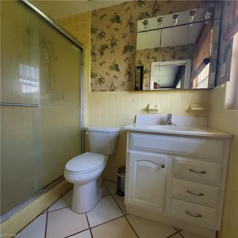 Bathroom with tile walls, vanity, a shower stall, wallpapered walls, and tile patterned floors