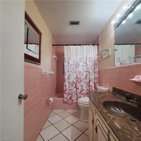 Full bath with tile walls, vanity, shower / bathtub combination with curtain, tile patterned flooring, and a wainscoted wall